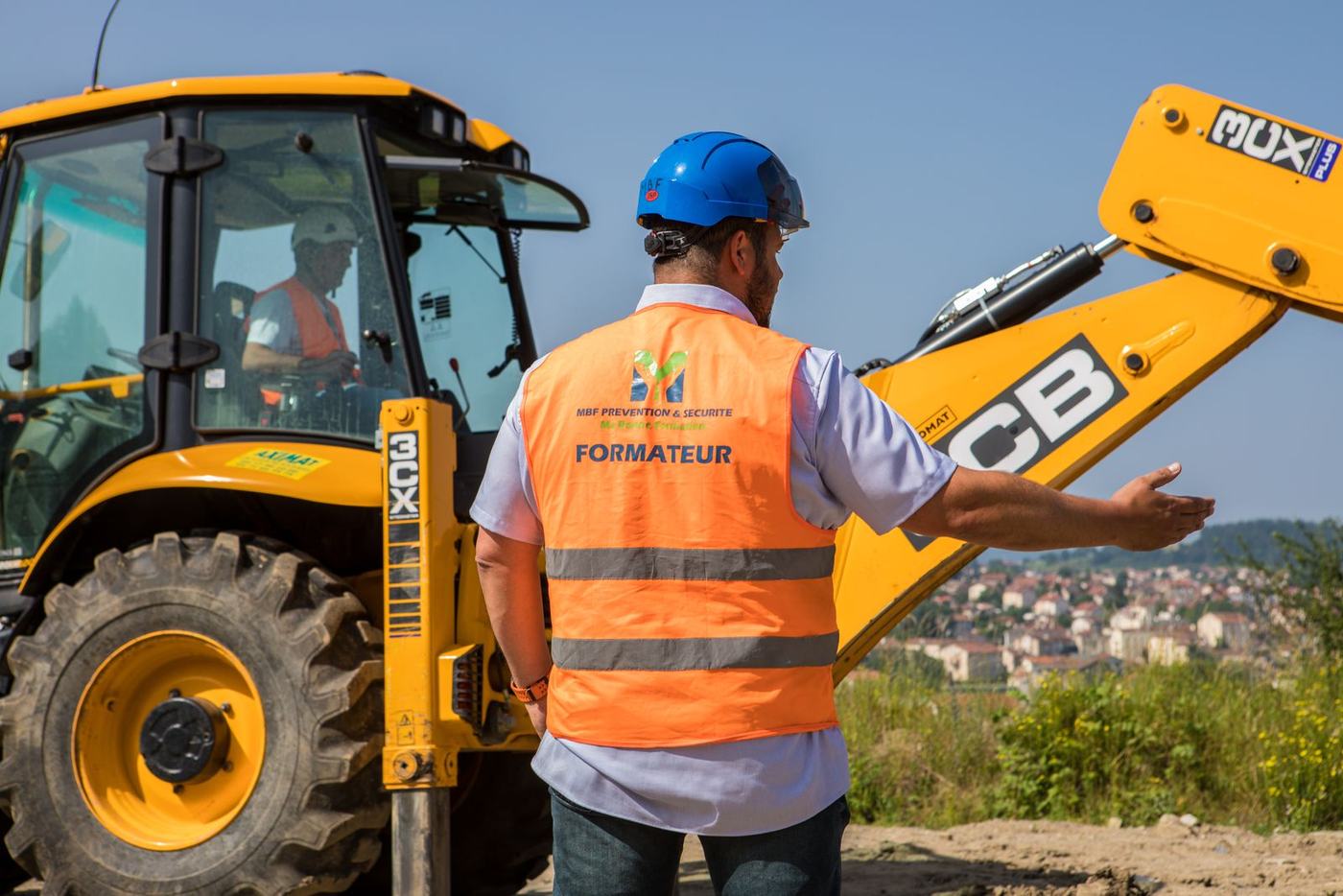 Formateur MBF donnant les consignes à un stagiaire sur chargeuse-pelleteuse JCB