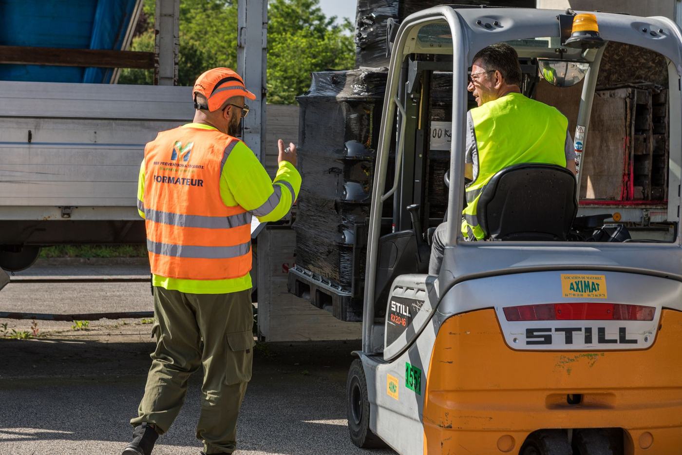 Formateur guidant un stagiaire lors d'une manœuvre en chariot élévateur à l'extérieur