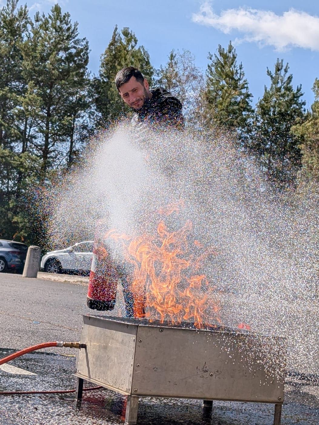 Stagiaire éteignant un feu réel sur bac à feu avec un extincteur à eau pulvérisée